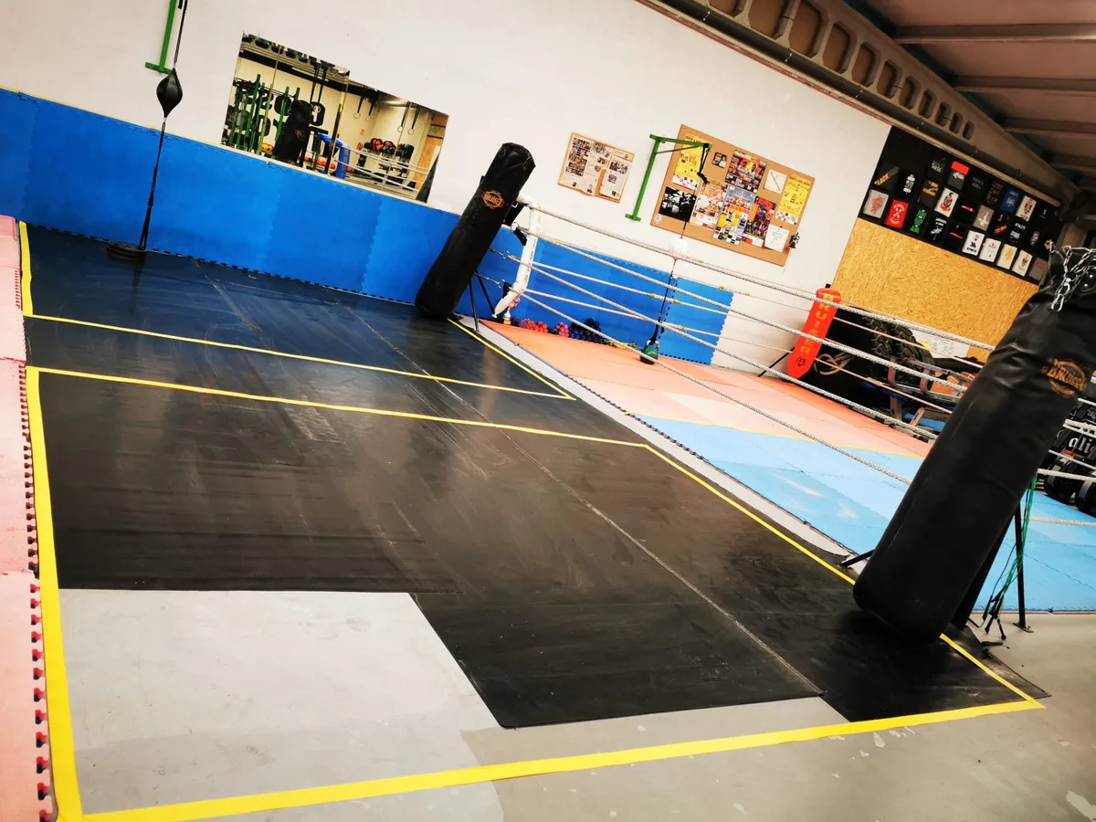 Tarima de entrenamiento con las distancias marcadas en amarillo, saco pesado y punching ball al fondo
